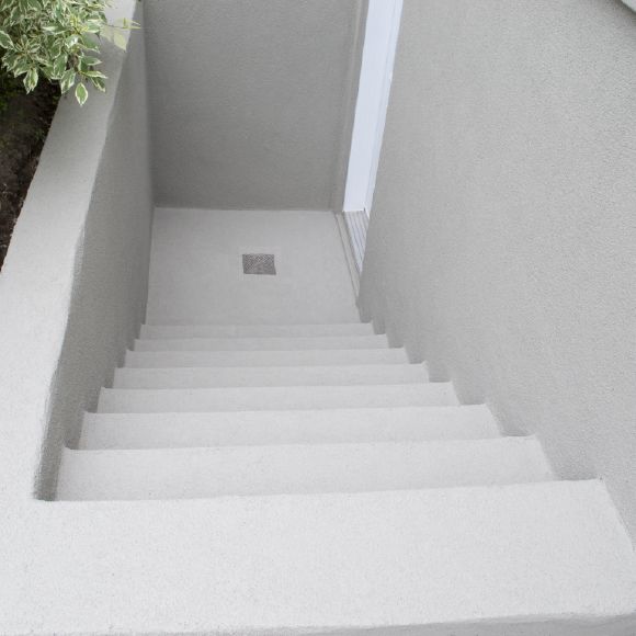 Finition en crépi acrylique sur descente d’escalier en béton extérieur.